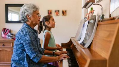 Older woman playing a piano duet with young girl